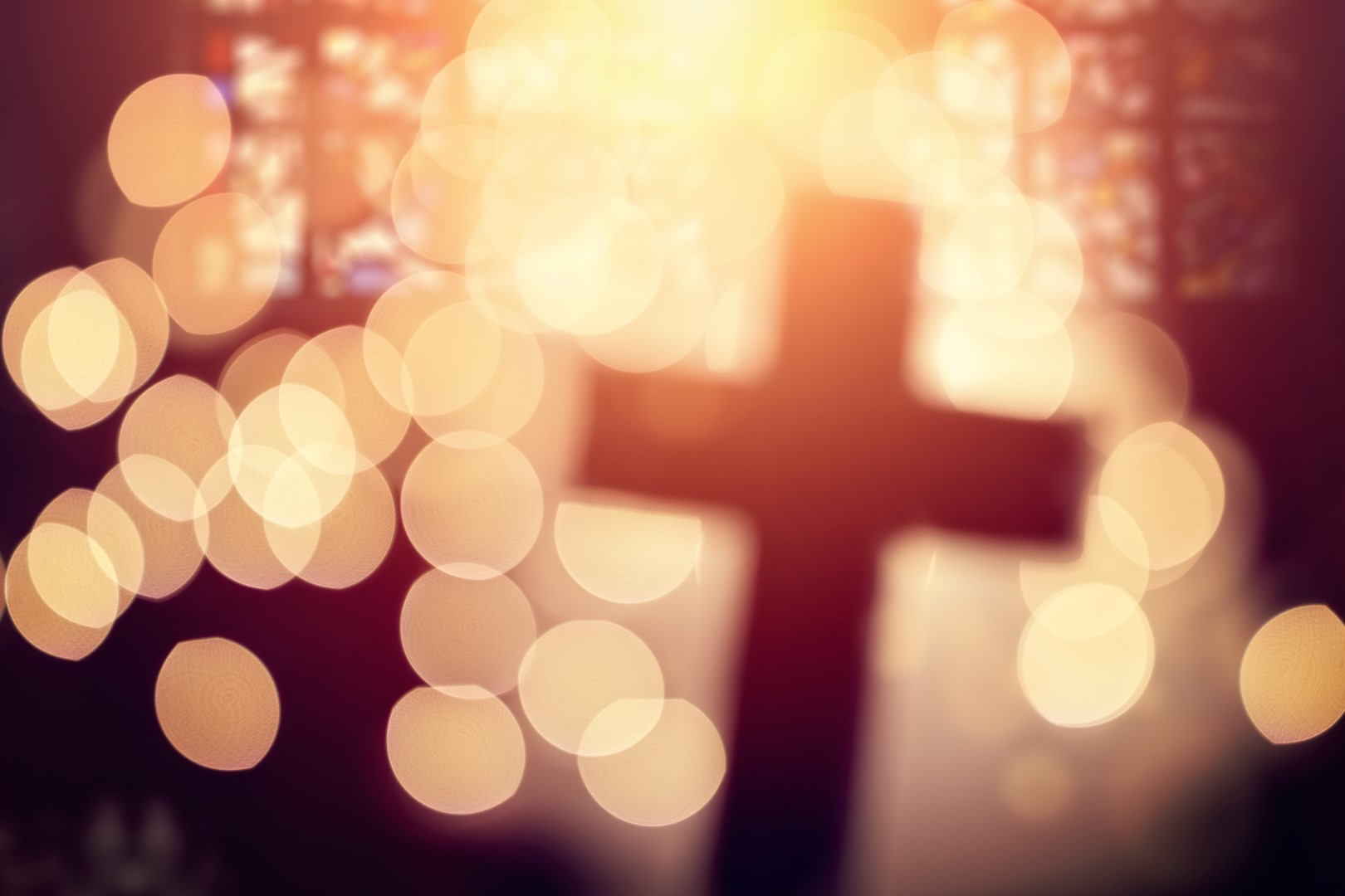 Abstract defocussed cross silhouette in church interior against stained glass window concept for religion and  prayer